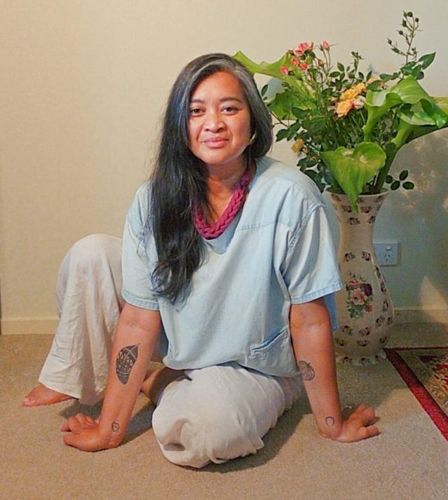 middle aged asian woman sitting on the floor. Flowers behind her.